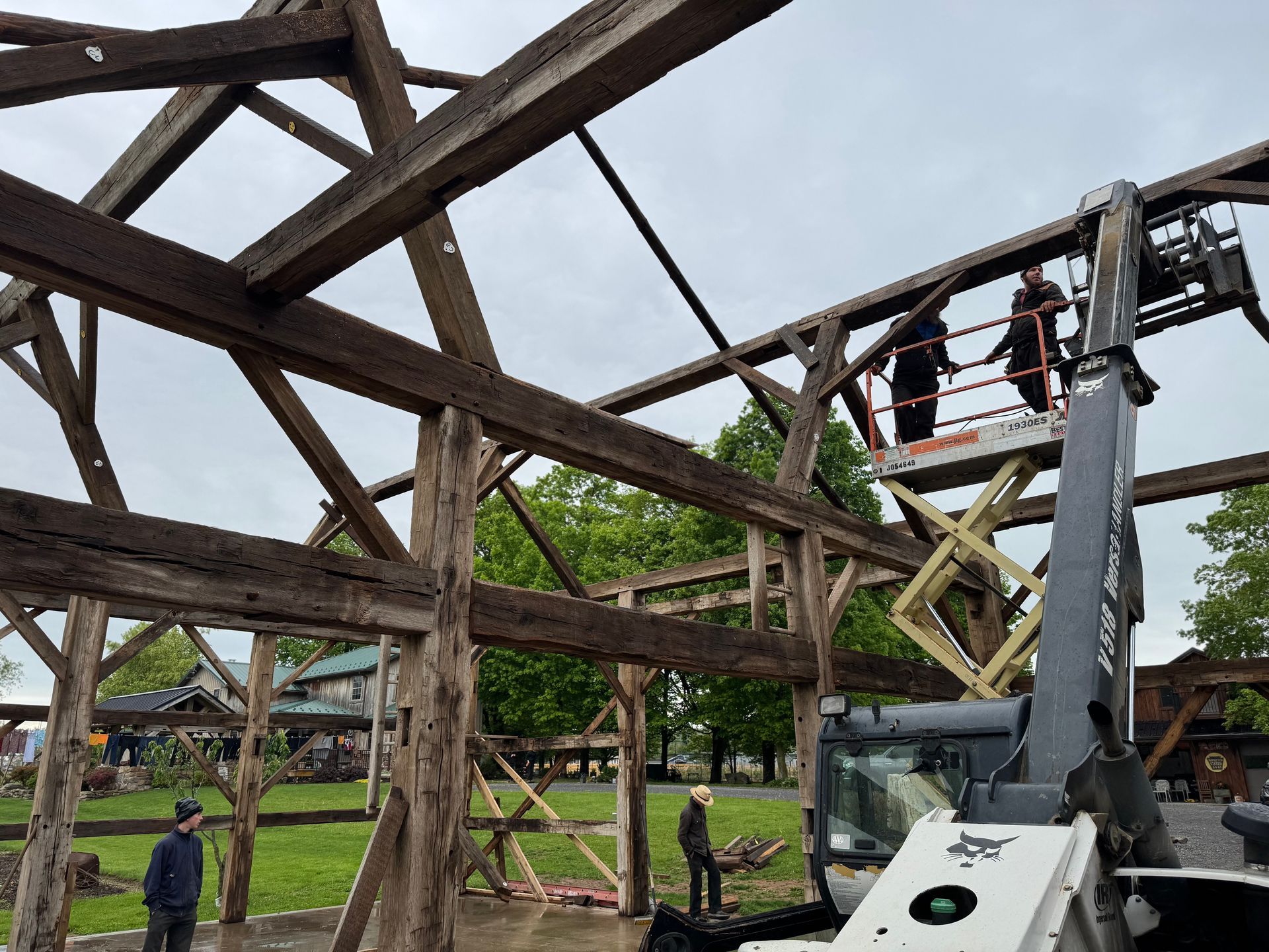 Workers on a scissor lift restoring a large timber frame, showcasing the craftsmanship of timber frame home builders.