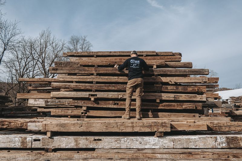 Worker inspecting reclaimed timber architecture materials outdoors.