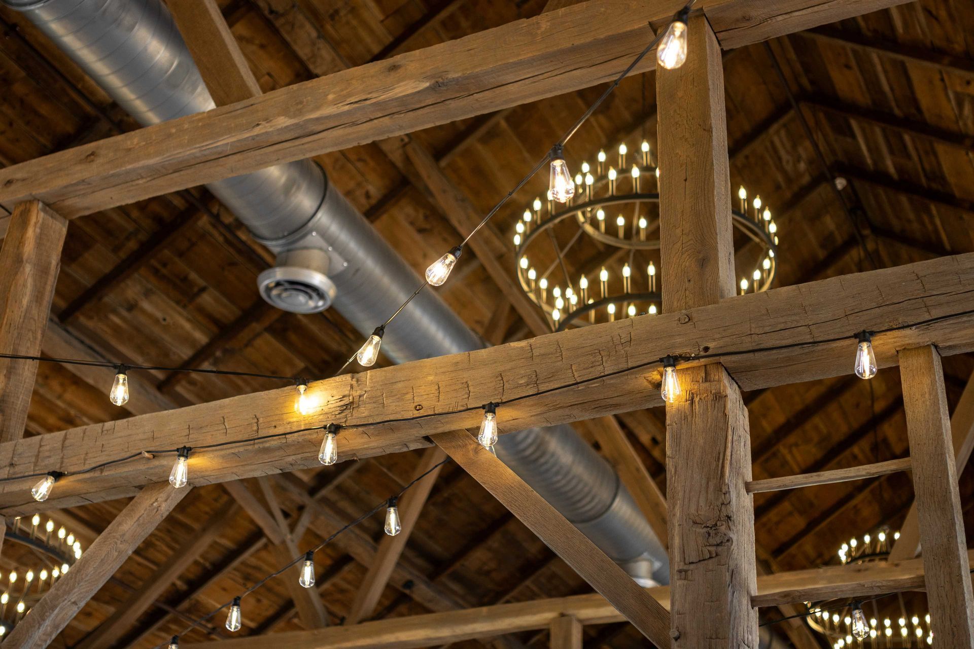 Barn ceiling with exposed wooden beams, chandeliers, and HVAC ducting, illustrating timber frame structural engineering.