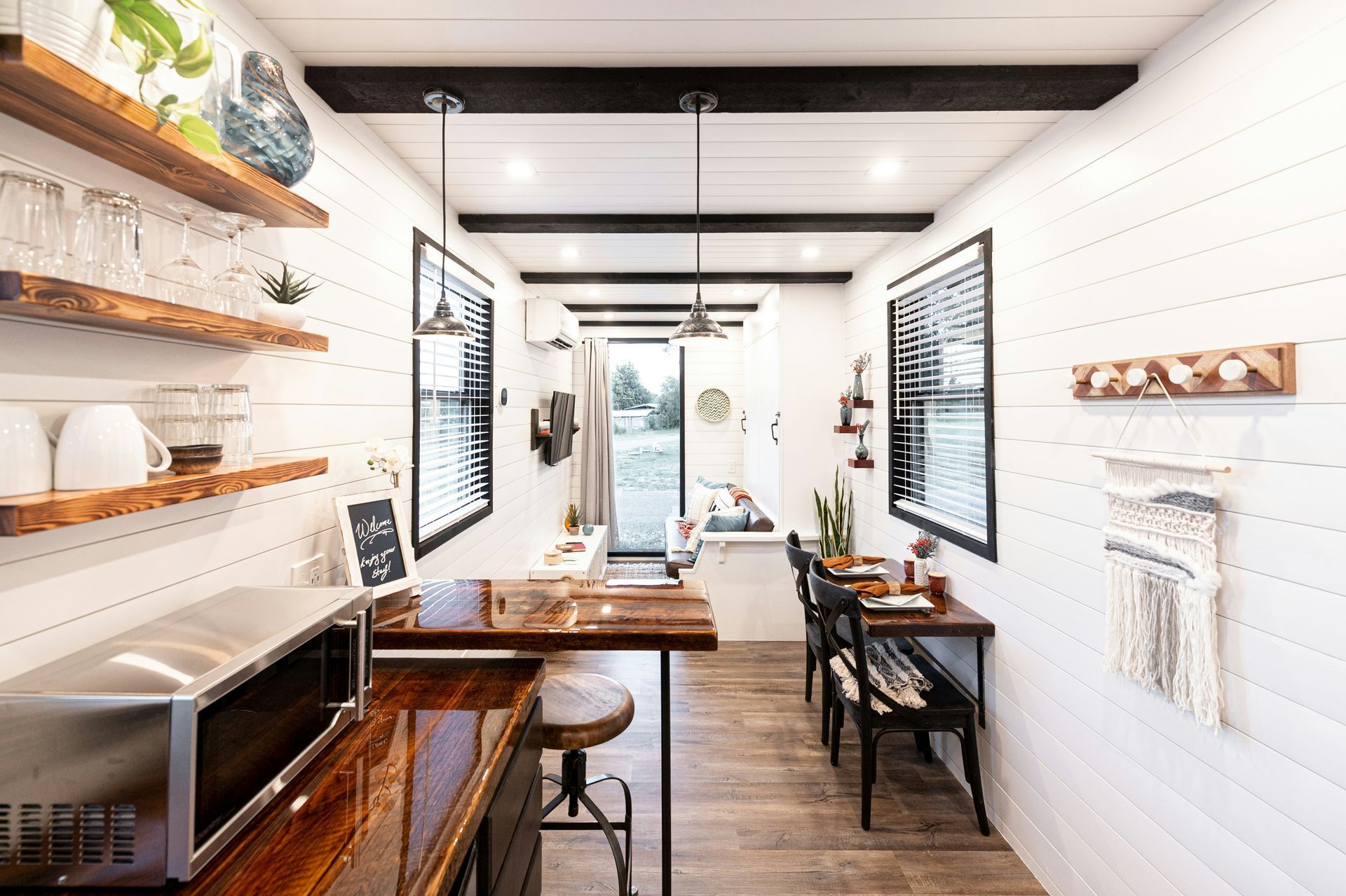 A container home with white shiplap walls, dark wood beams, reclaimed wood countertops, and an open kitchen-dining layout.