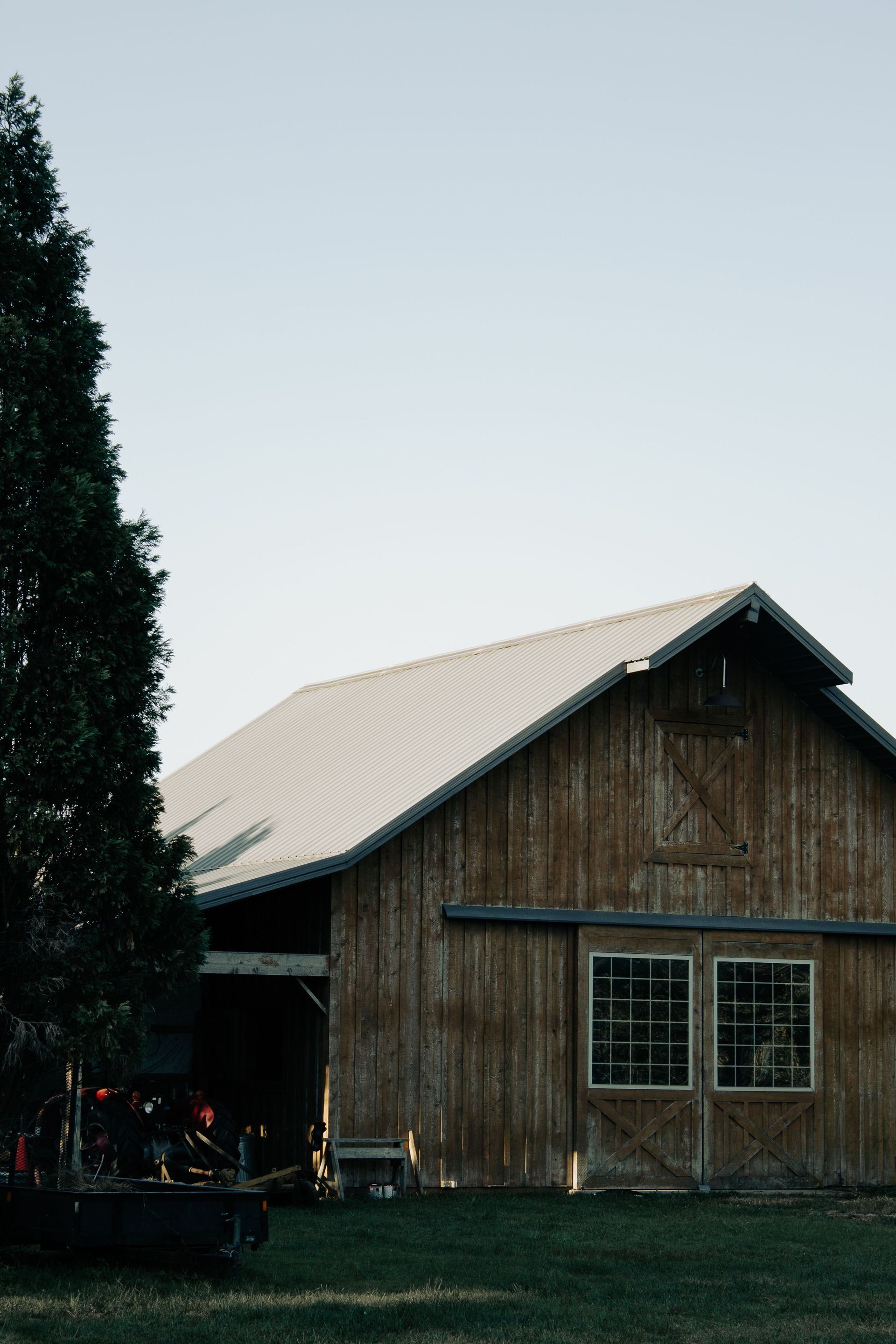 Rustic wooden barn with a light metal roof beside a tall tree on a grassy lawn in Pennsylvania.