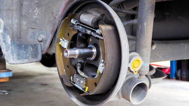 A close-up view of an automobile's rear drum brake assembly, showing the brake shoes and hub with a removed wheel.