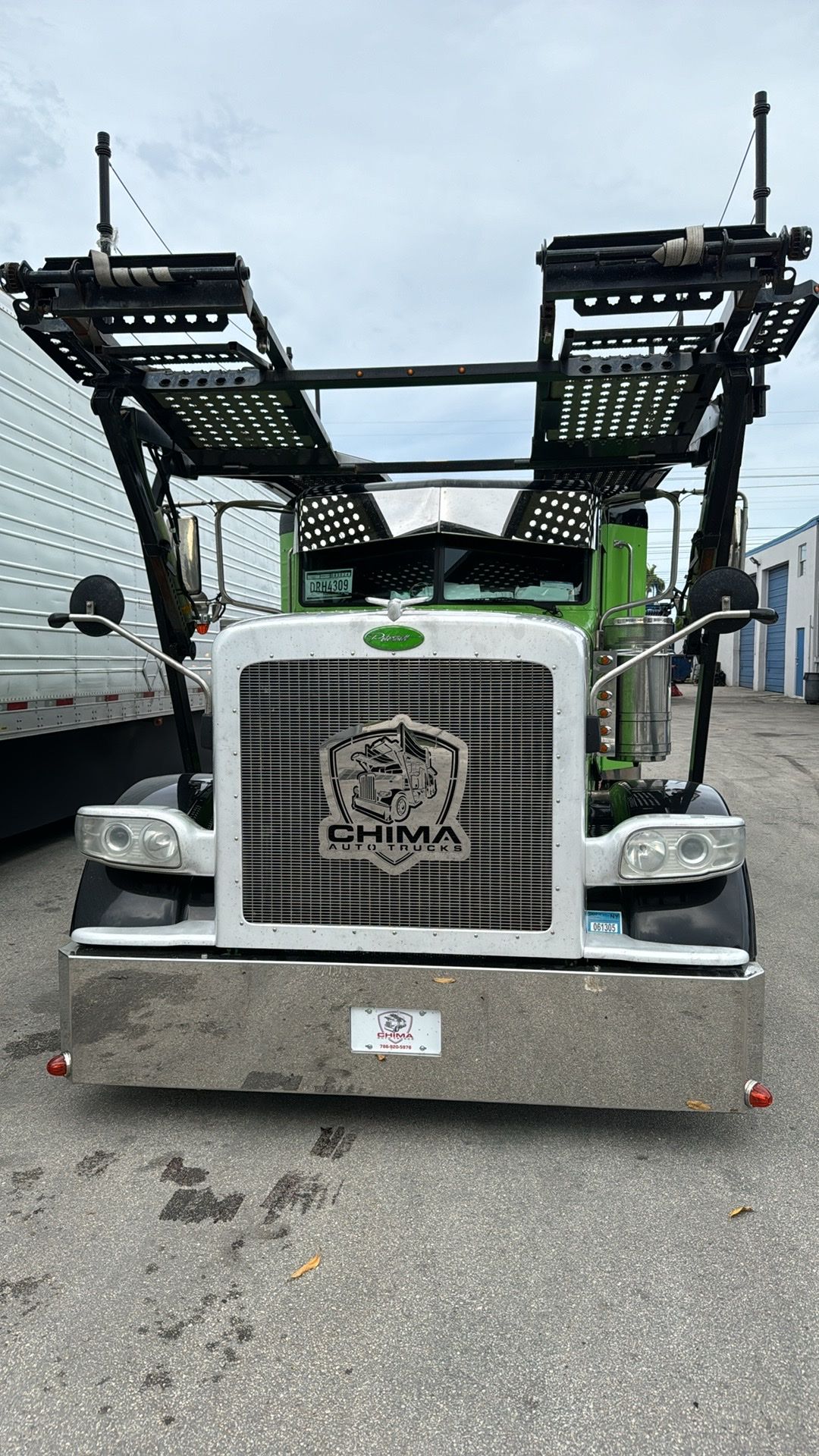 Front view of a bright green and white auto hauler truck with a large, decorative shield emblem on the grille.