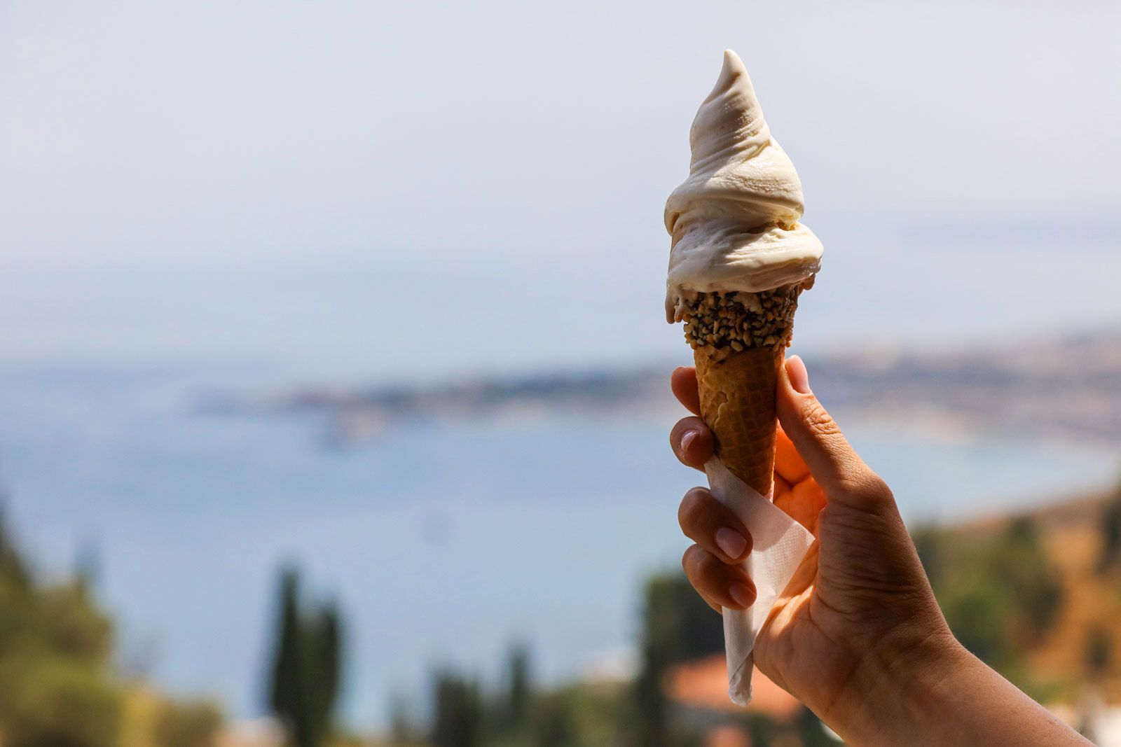 Mano che regge un cono gelato con vista sul mare sullo sfondo.