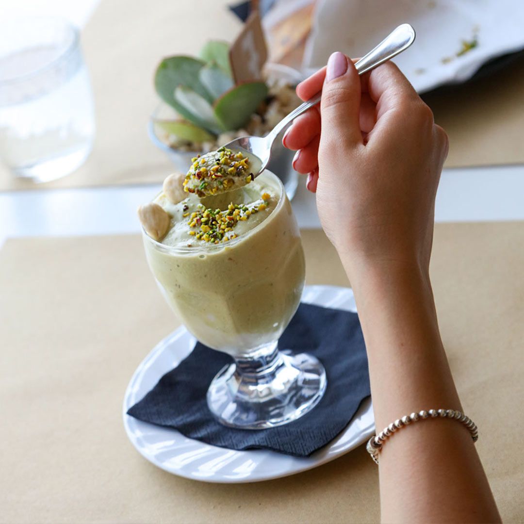 Una persona prende un dessert al pistacchio da un bicchiere con un cucchiaio.