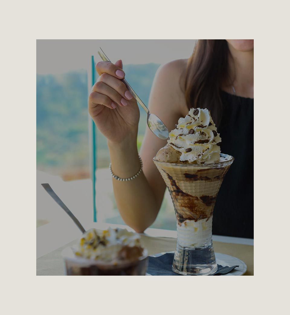 Donna che mangia una coppa di gelato in un bicchiere alto, all'aperto.