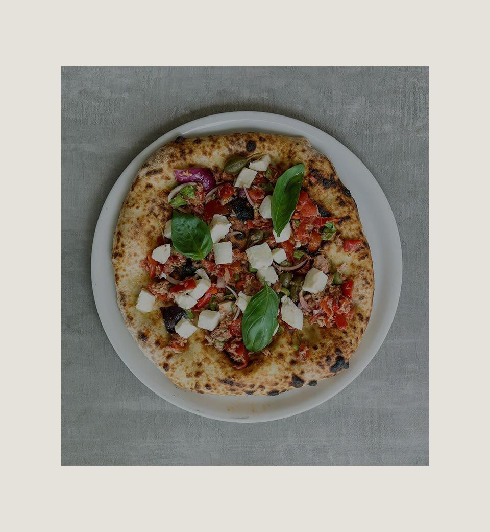 Pizza con basilico, pomodori e formaggio su un piatto bianco.