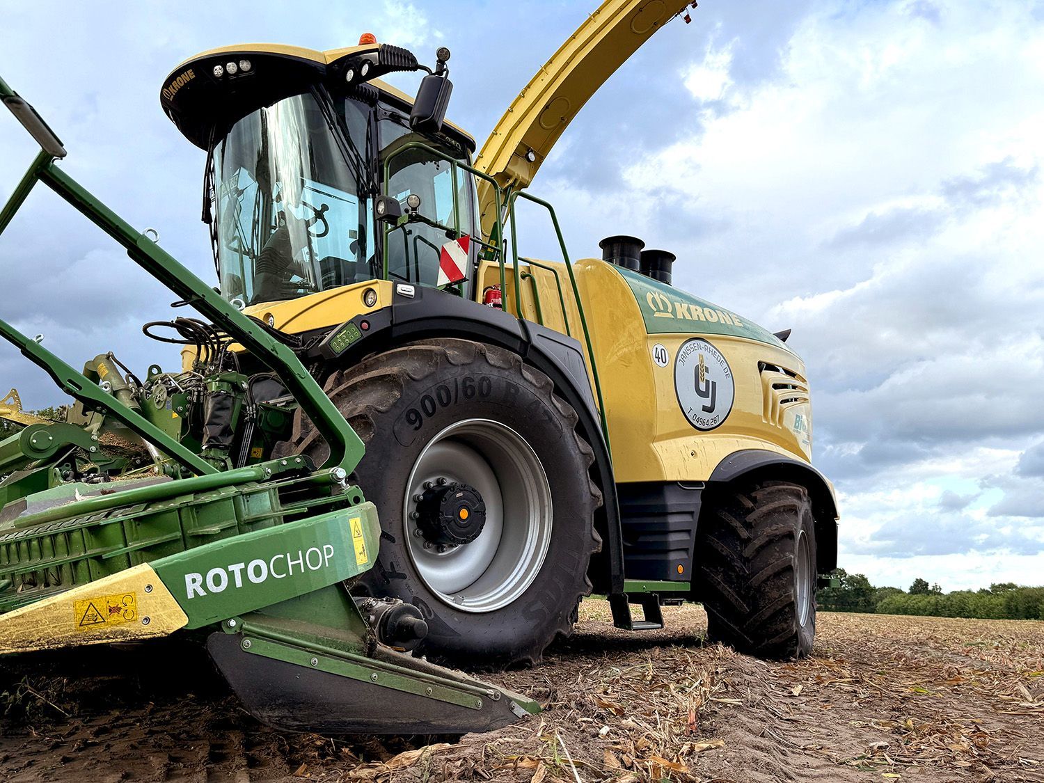 Gelbe Erntemaschine mit grünem Schneidwerk auf einem Feld, von der Seite gesehen