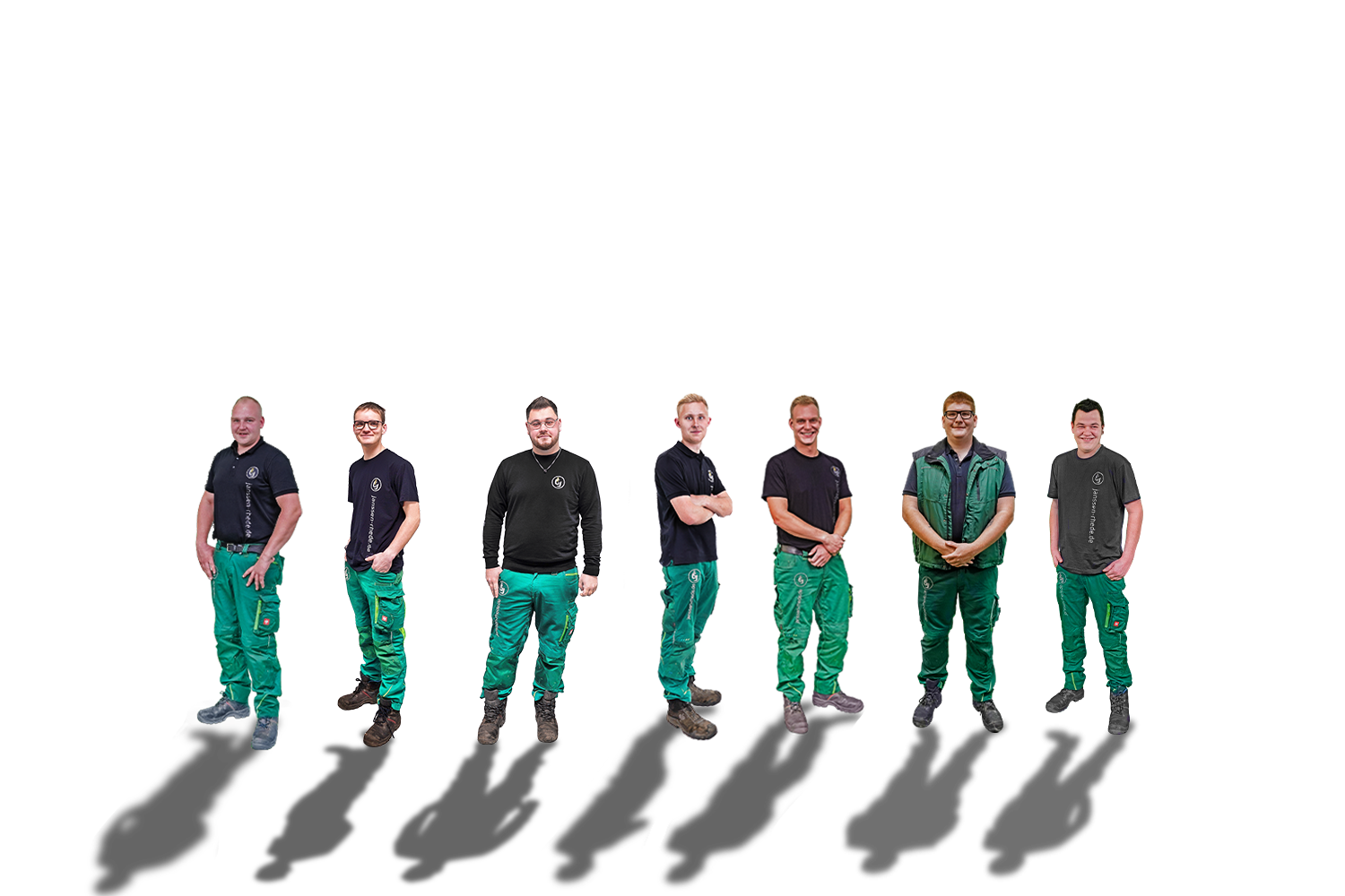 Acht Personen stehen in einer Reihe vor einem weißen Hintergrund; alle tragen grüne Arbeitshosen und dunkle Hemden oder Jacken.