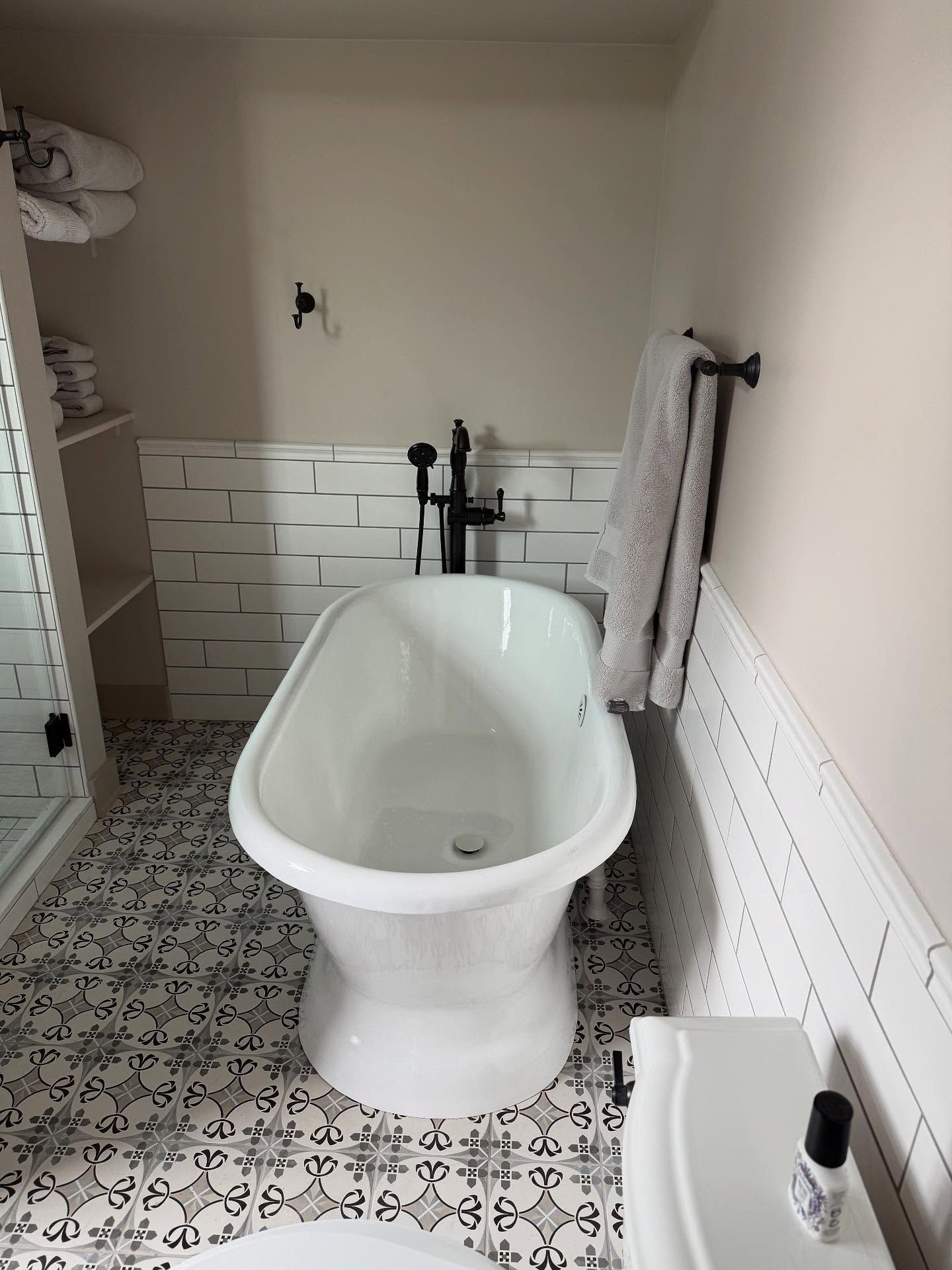 Small bathroom with a white freestanding tub, patterned tile floor, and built-in drawers.