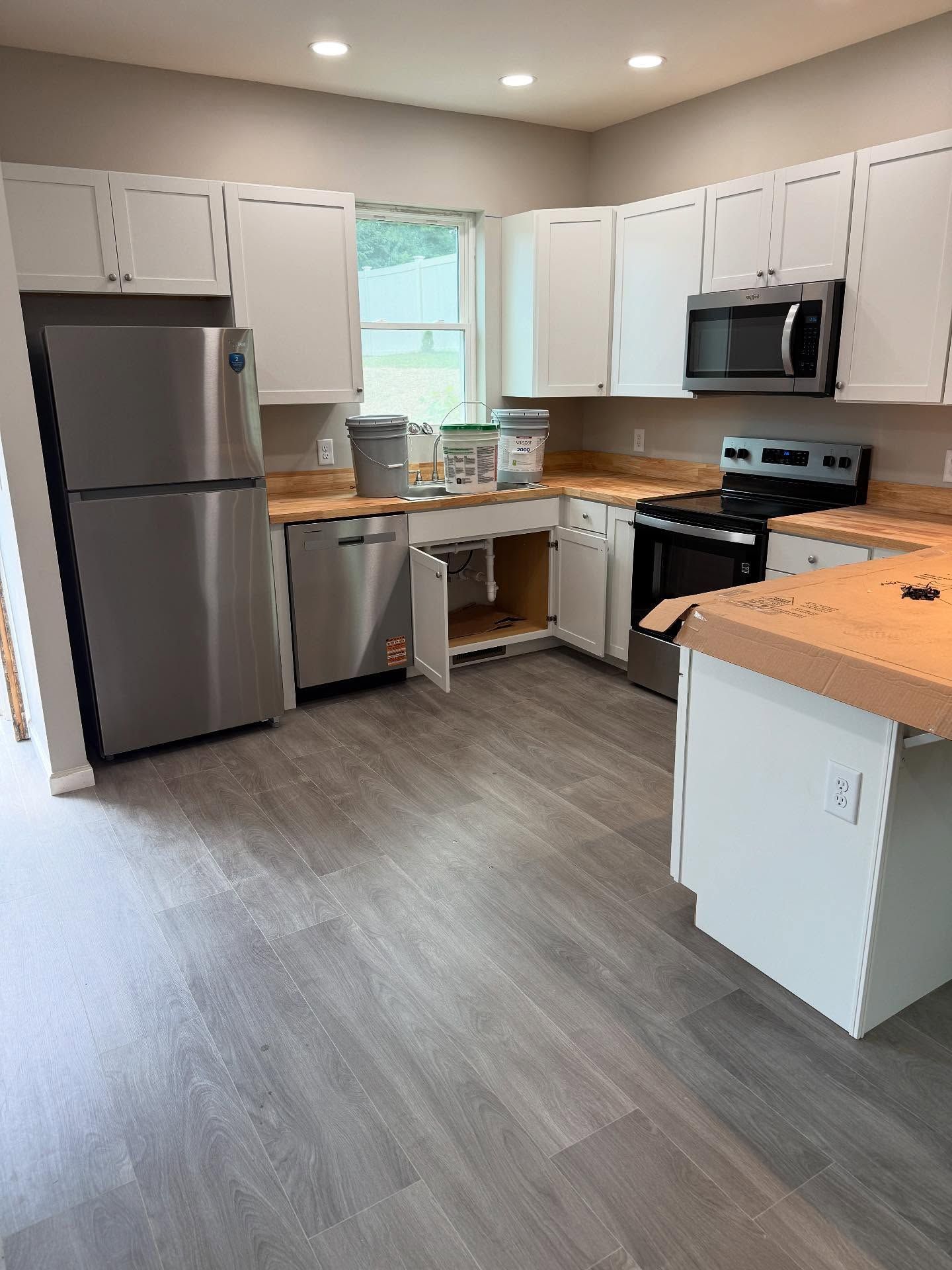Bright kitchen with white cabinets, stainless appliances, gray floor, and wood countertops around a window sink.