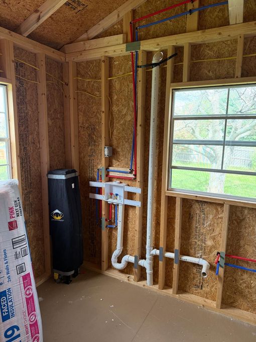 Unfinished wall framing with exposed plumbing pipes, a black water heater, and a window in a construction space