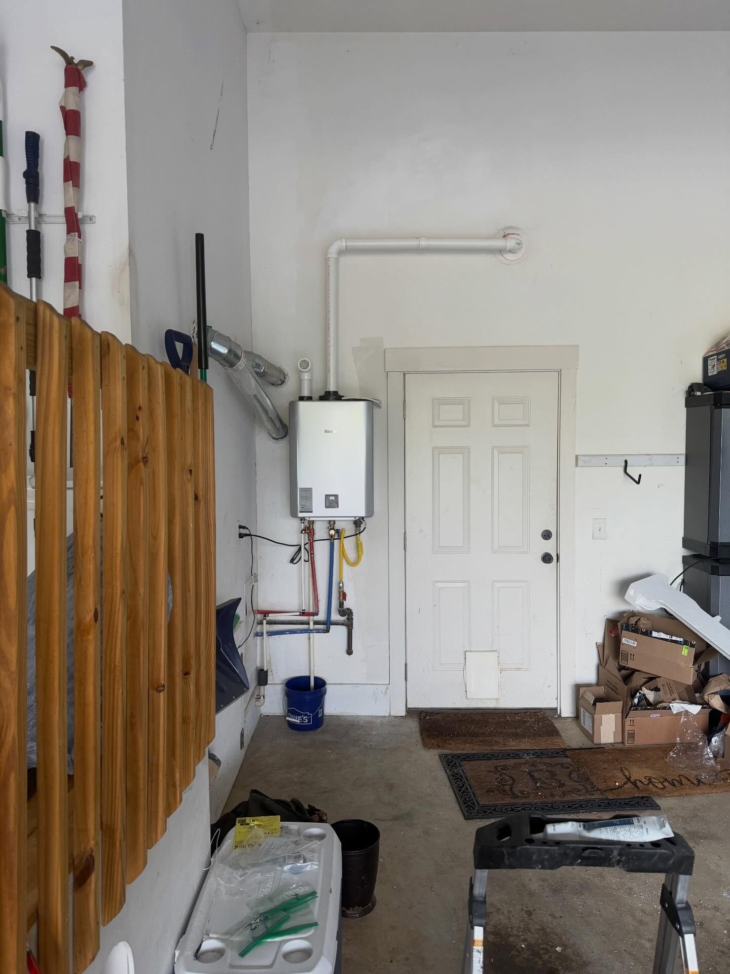 Garage interior with boiler, white door, wooden fence panels, and stored boxes along the wall