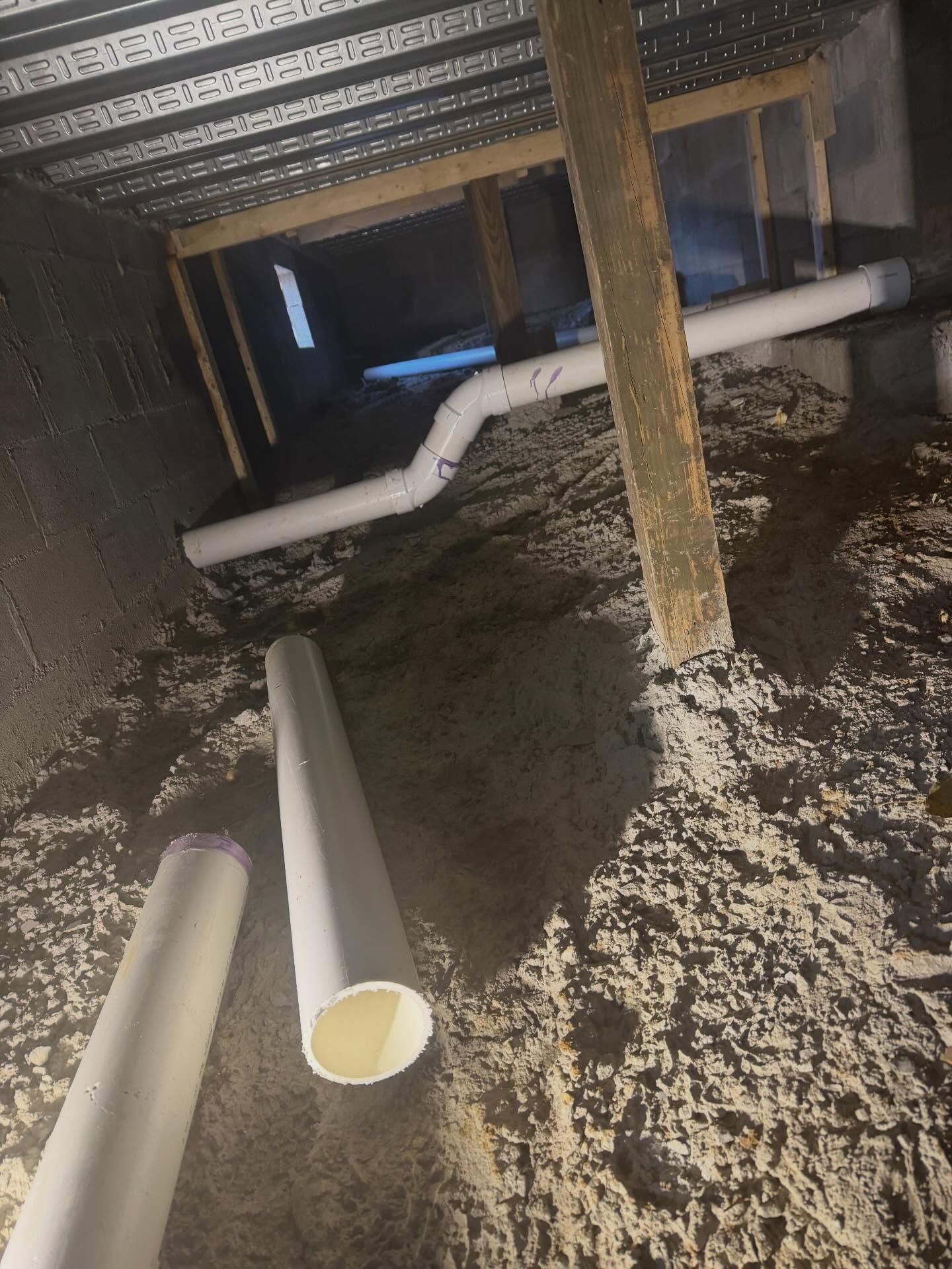 Dim crawlspace with white PVC pipes and a wooden support post on a dirt floor.