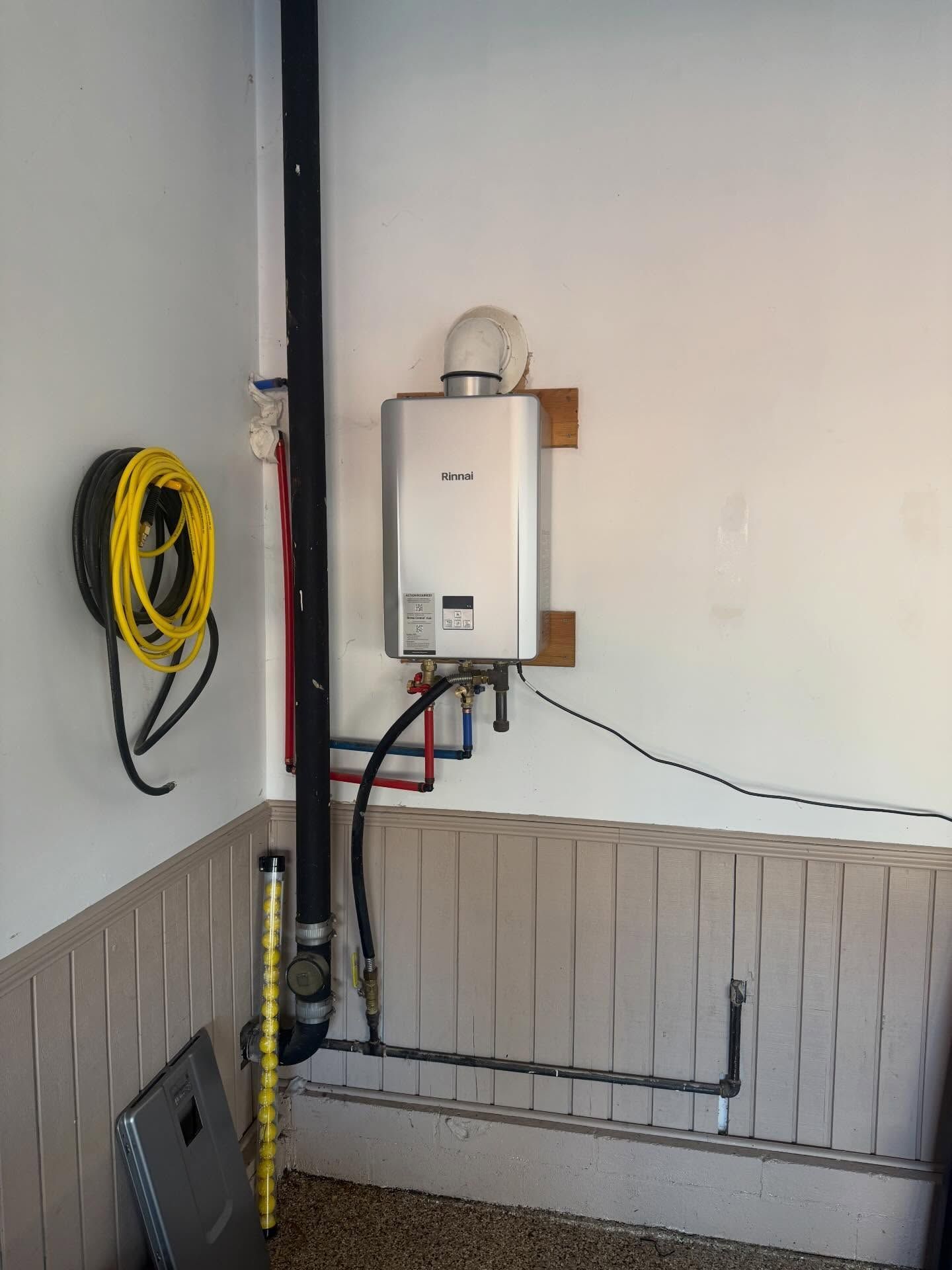 Wall-mounted boiler with pipes and coiled yellow hose in a utility room