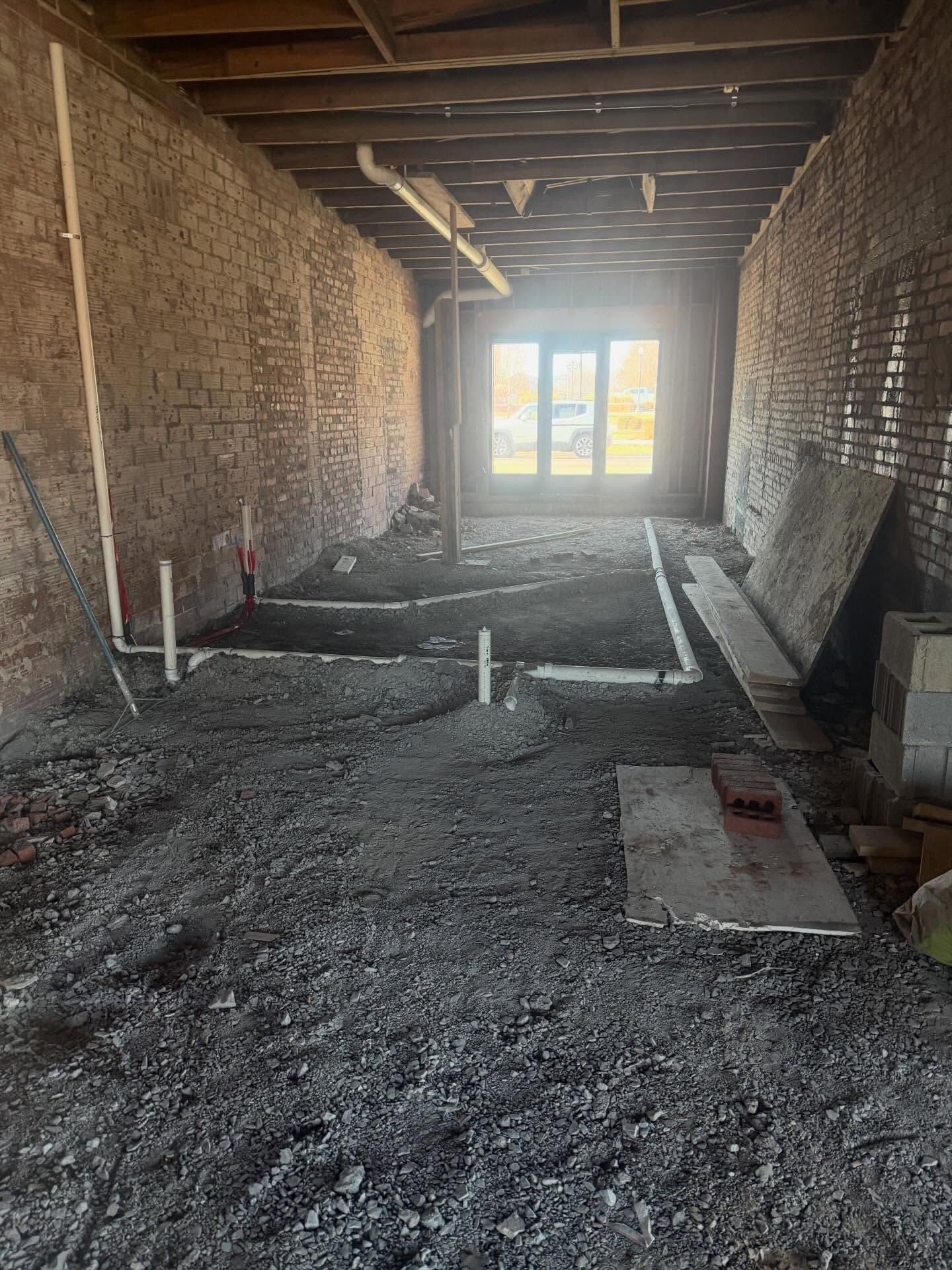 Unfinished interior room with gravel floor, exposed brick walls, and bright double doors at the far end.