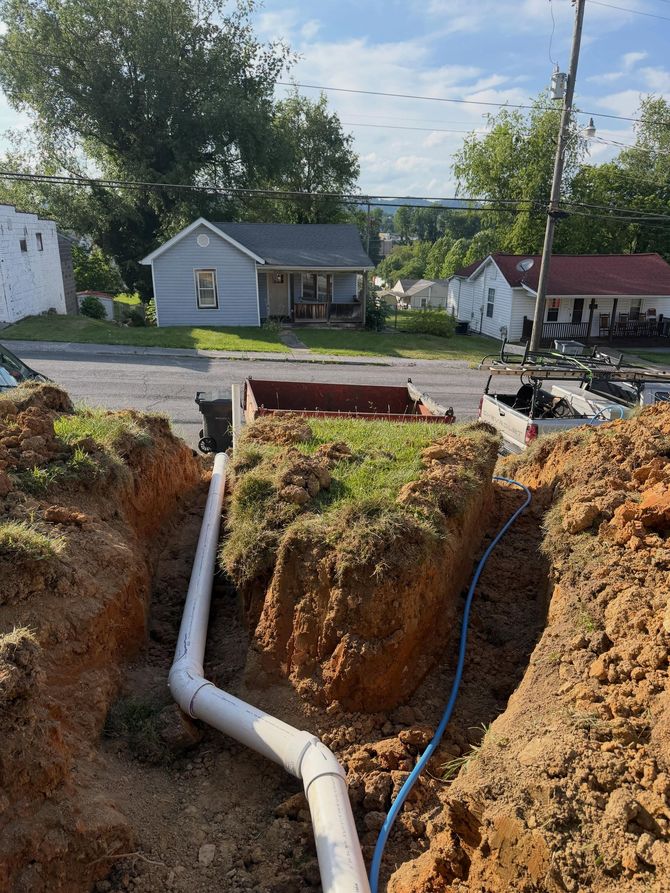 Trenched utility pipe installation with white PVC pipe leading to a street-side excavation site