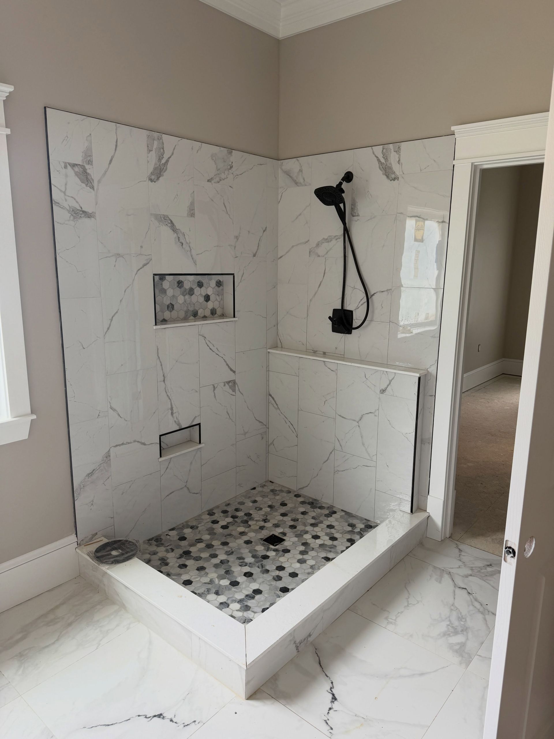 Walk-in shower with marble-look tile walls and floor, built-in bench, and black shower fixtures.