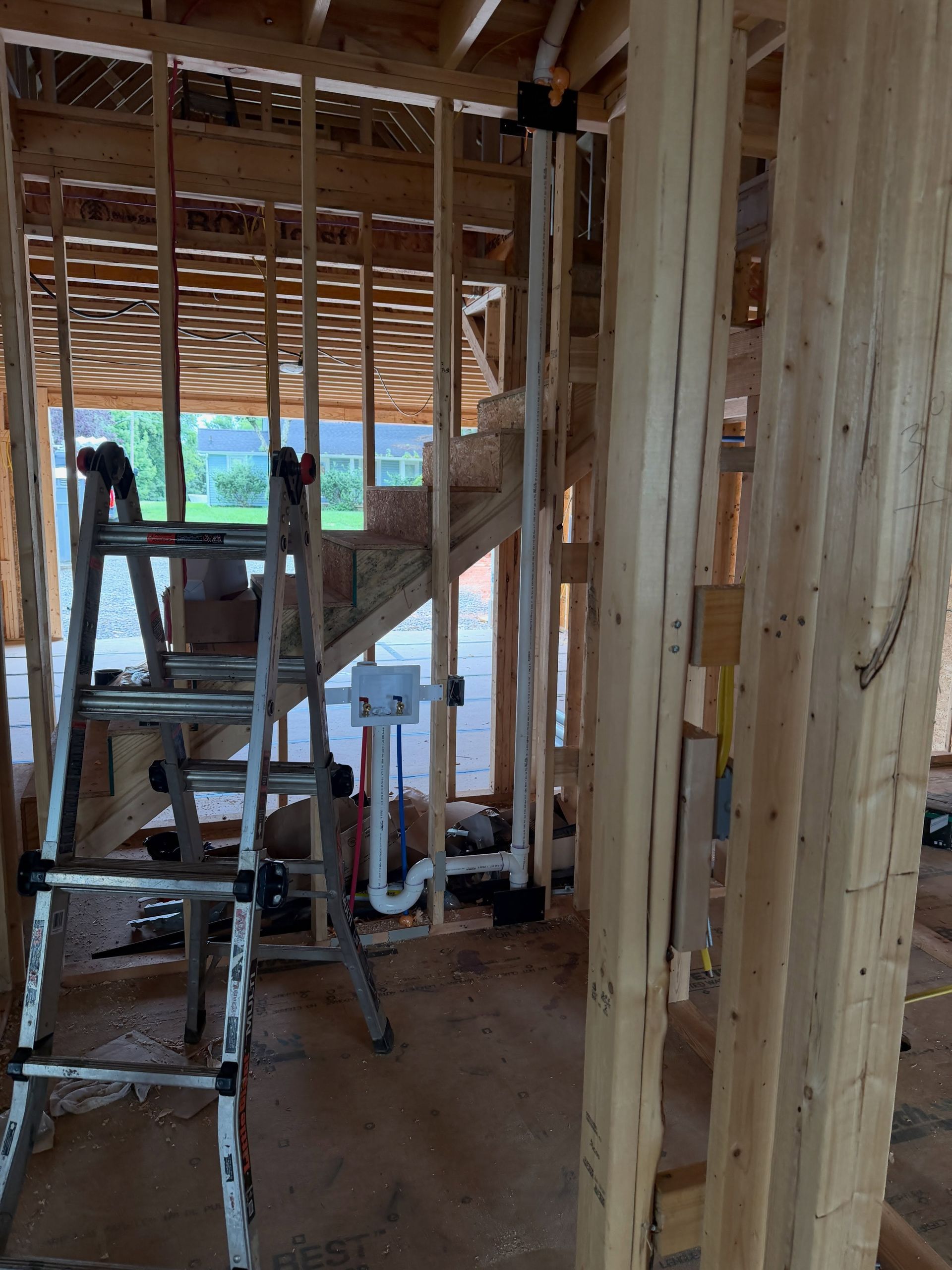 Construction site interior with ladder, scaffolding, exposed framing, and plumbing pipes