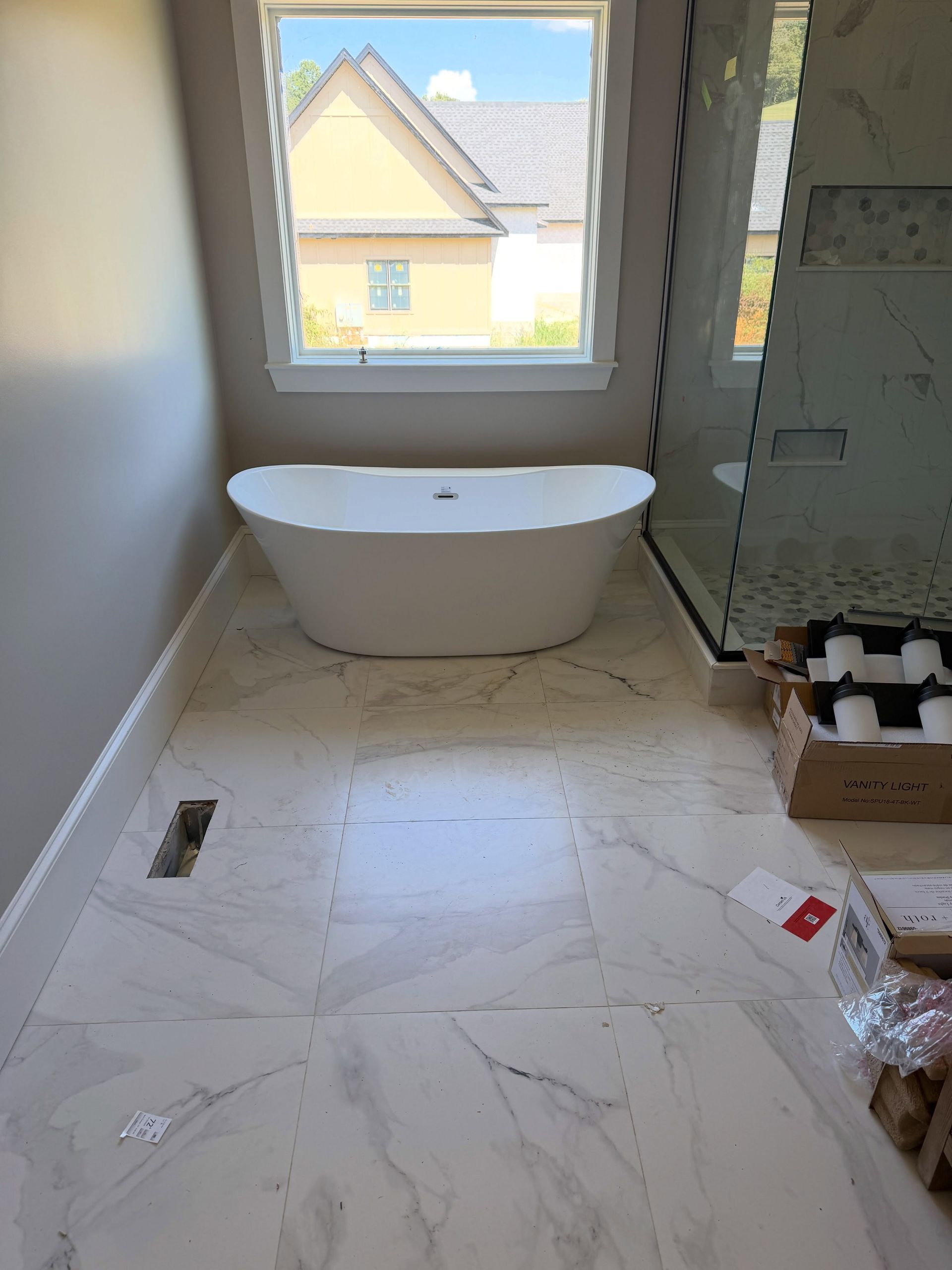 Partially renovated bathroom with a freestanding tub, white tile floor, and a window above it
