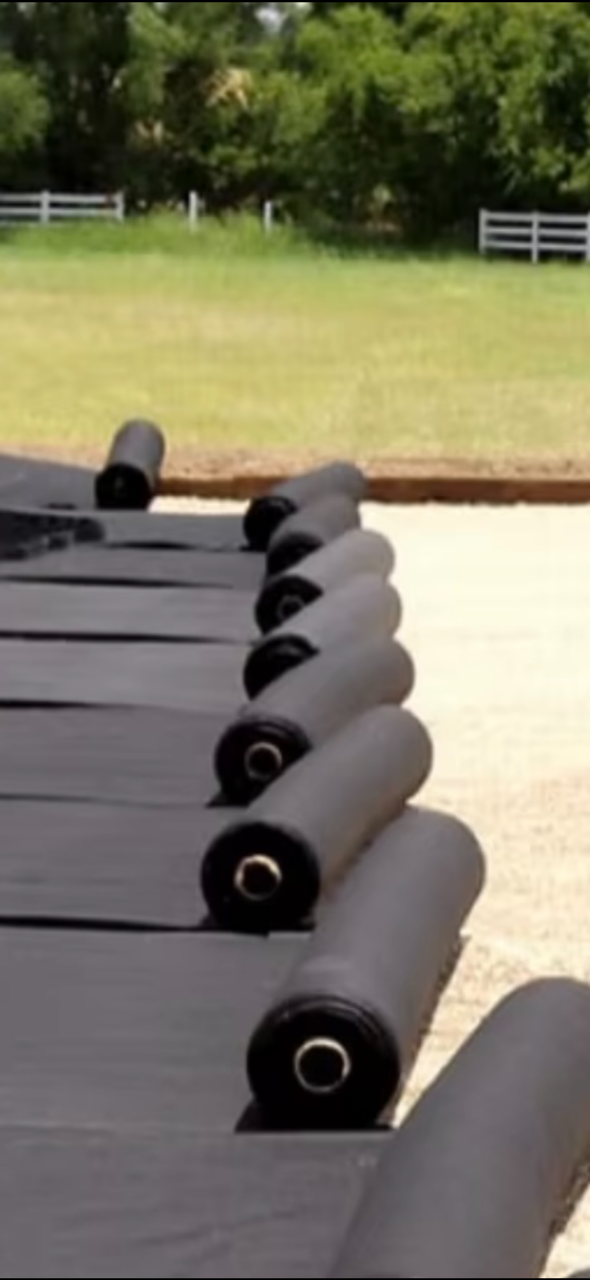 Rolled black outdoor mats lined up on a patio beside a lawn and white fence