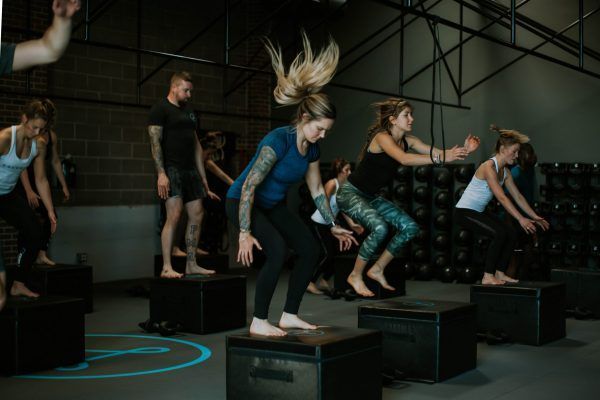 People jumping on boxes in a gym. Dark setting with people wearing athletic clothing.