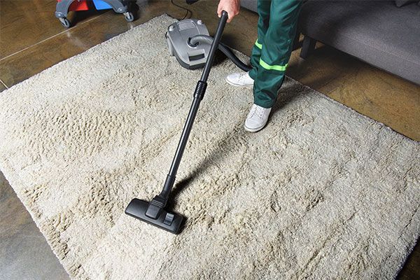 Person vacuuming a light beige rug with a black vacuum cleaner.