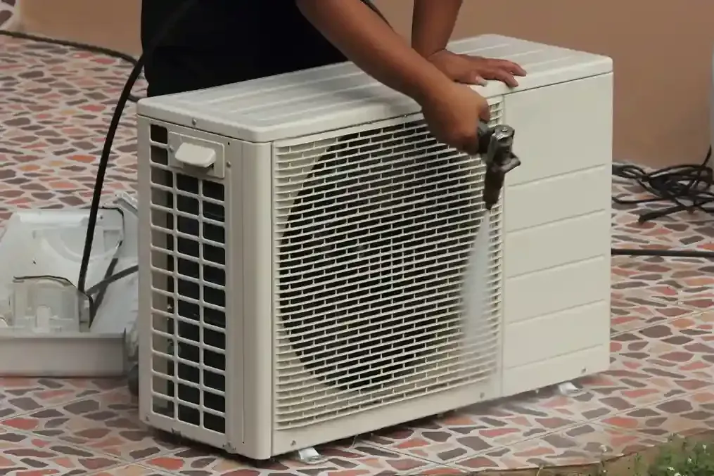 Person spraying an outdoor heat pump unit with water.