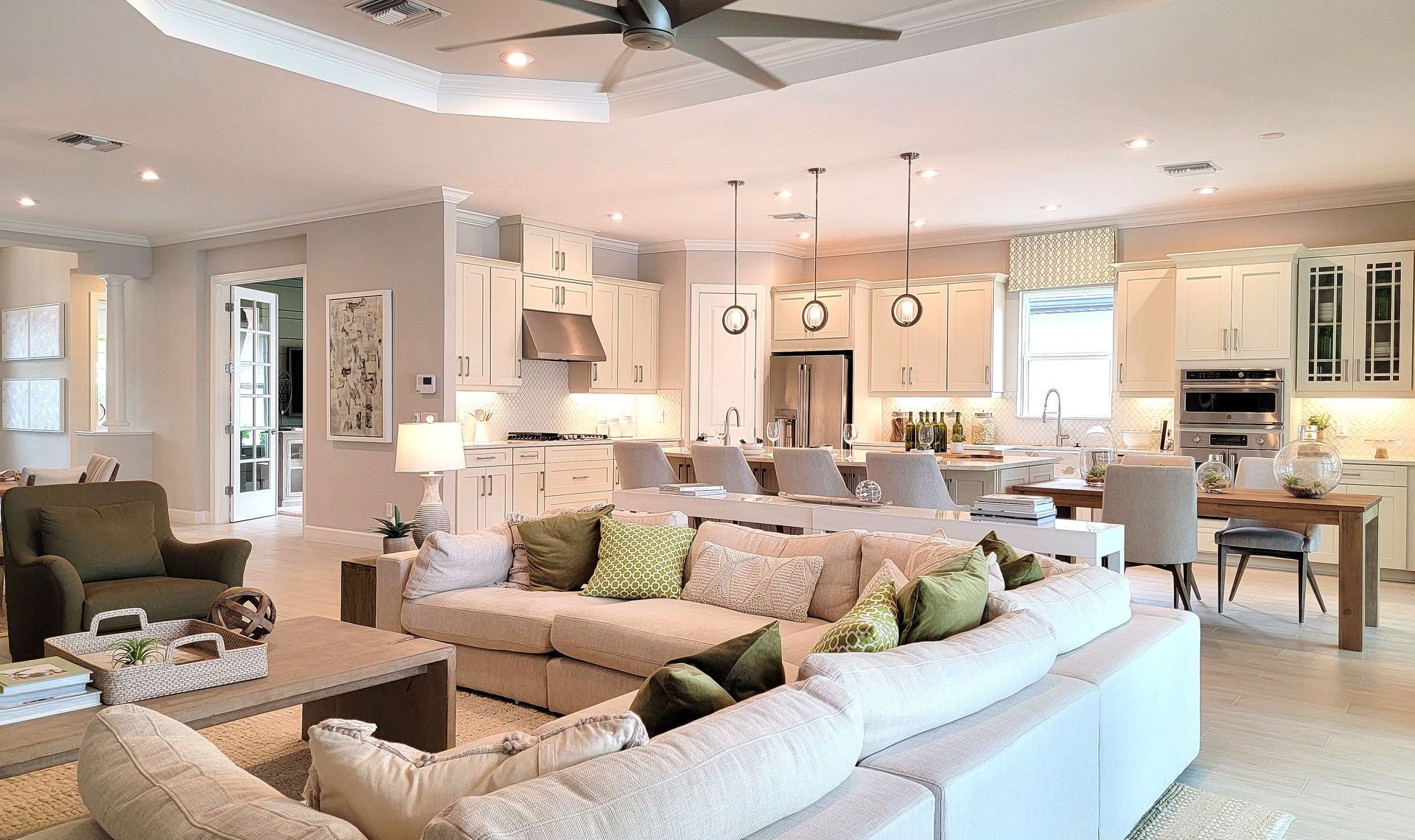 Bright open-concept living room and kitchen with white furniture, beige decor, and pendant lights