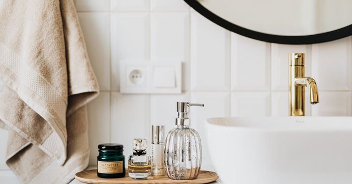 Bathroom vanity with white sink, gold faucet, black mirror, and toiletries on a wooden tray