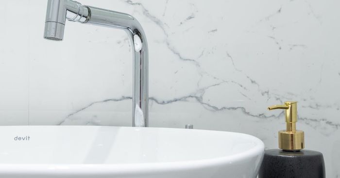 Modern bathroom sink with chrome faucet, white basin, and black soap dispenser on marble wall background
