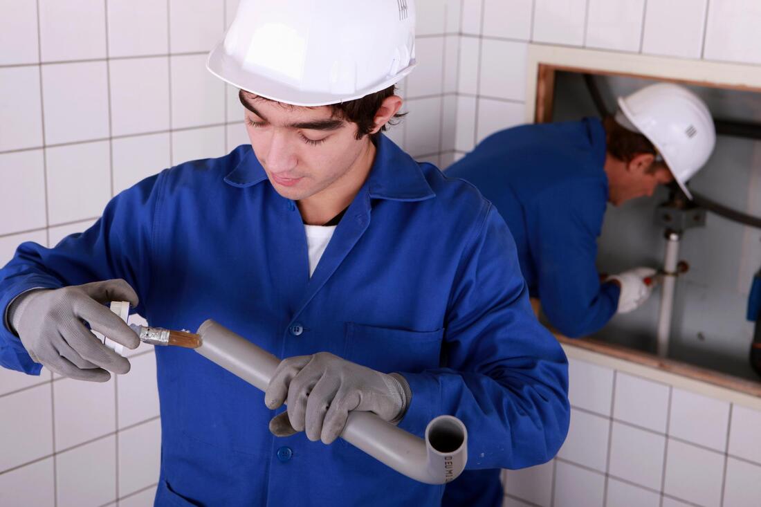 Worker in blue uniform inspecting a pipe with a wrench in a tiled utility room