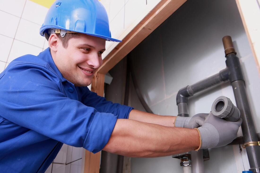 Plumber in blue uniform and hard hat tightening pipes under a sink