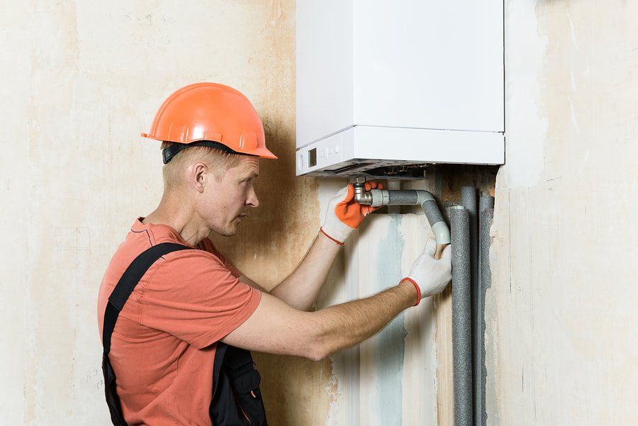 Technician in orange hard hat inspecting pipes under a wall-mounted boiler