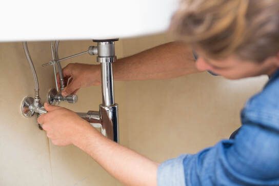 Person working under a sink with a wrench on plumbing pipes