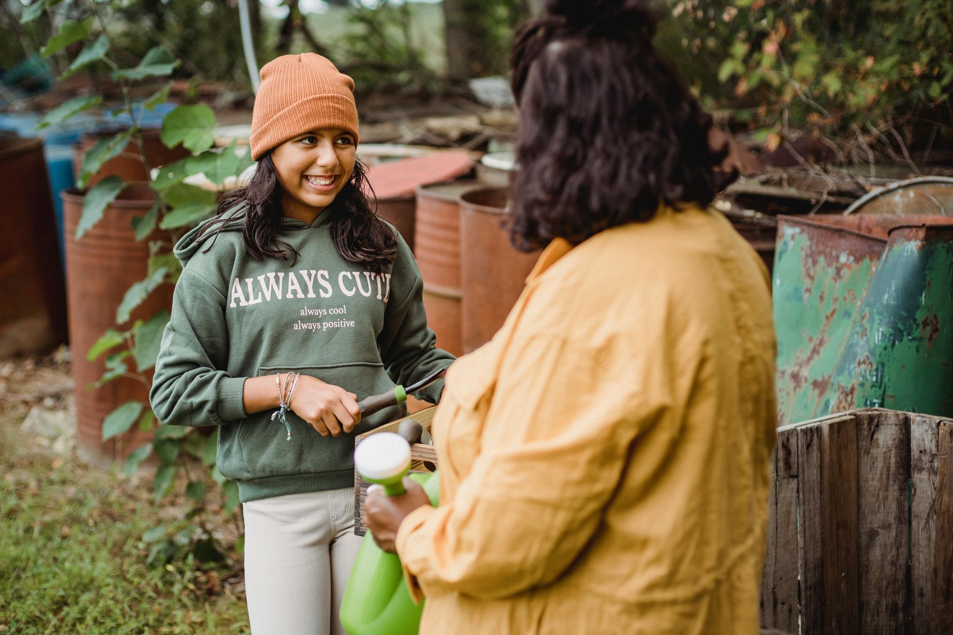 A woman is talking to a young girl who is holding a watering can.