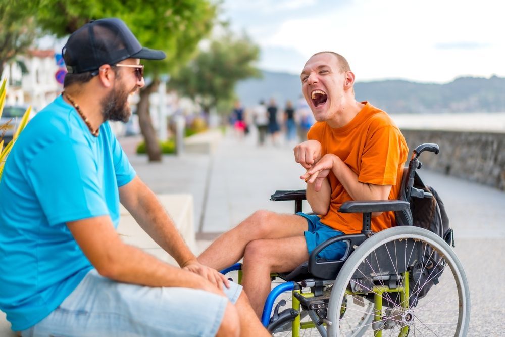 A Man Is Sitting Next To A Man In A Wheelchair — Comfort N Care Support QLD Pty Ltd In Dalby, QLD