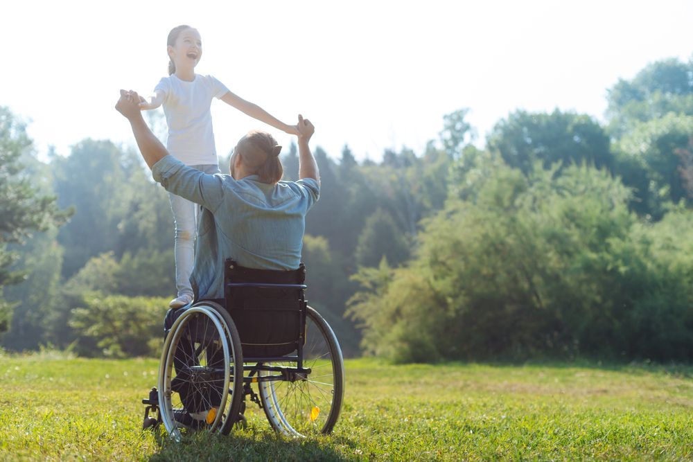 A Man In A Wheelchair Is Holding The Hands Of A Little Girl — Comfort N Care Support QLD Pty Ltd In Roma, QLD