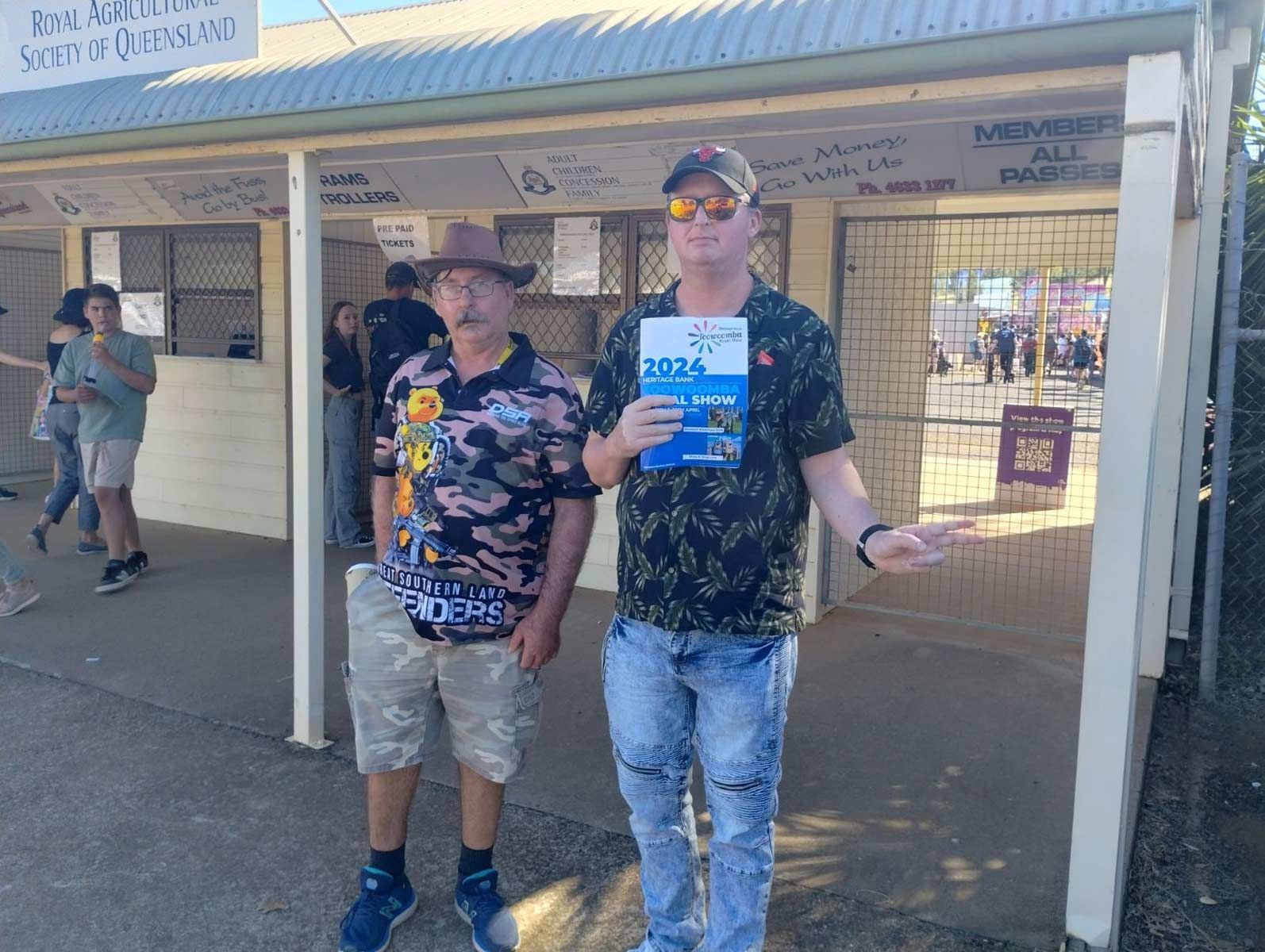 Two Men Are Standing Next to Each Other in Front Of a Building Holding a Book — Comfort N Care Support QLD Pty Ltd In Toowoomba City, QLD