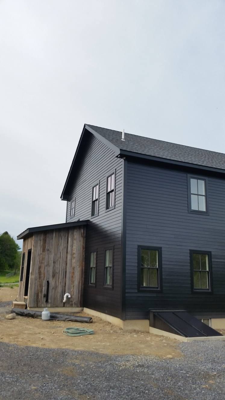 A large black house with a lot of windows is sitting on top of a dirt field.