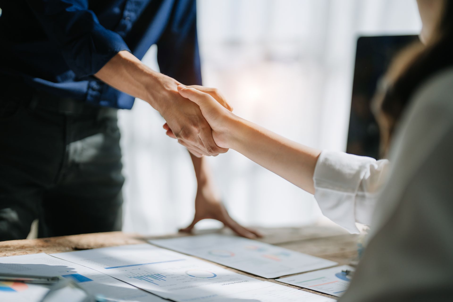 A man and a woman are shaking hands over a table.