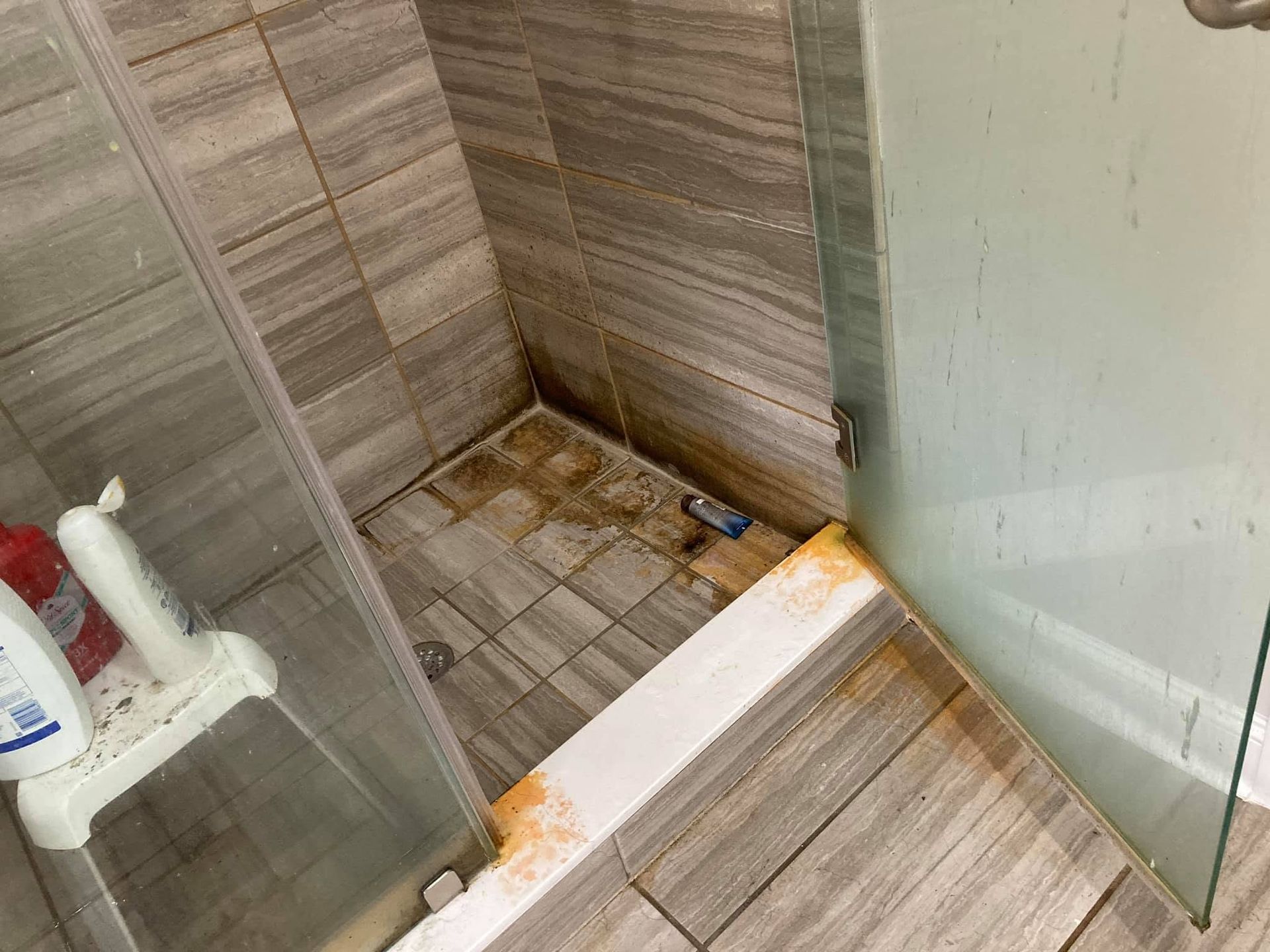 Small tiled shower stall with a glass partition and exposed, unfinished floor area near the drain.