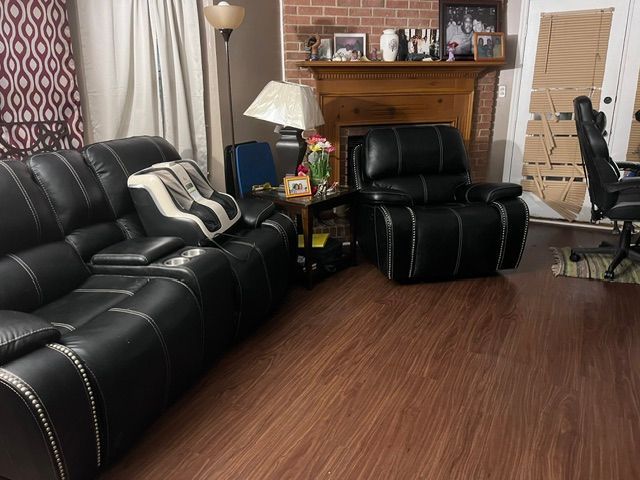 Living room with black leather sofa and recliner, wood floor, fireplace, and curtains