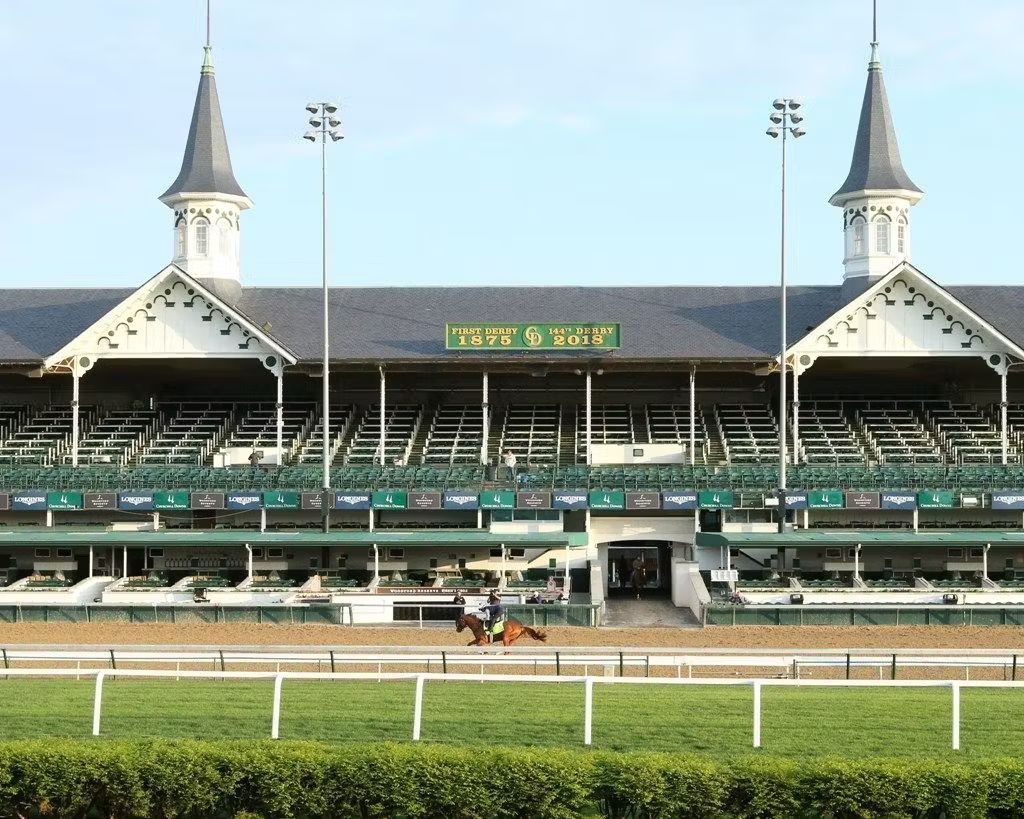 Horse racetrack grandstand with twin spires, green infield, and a few horses on the track