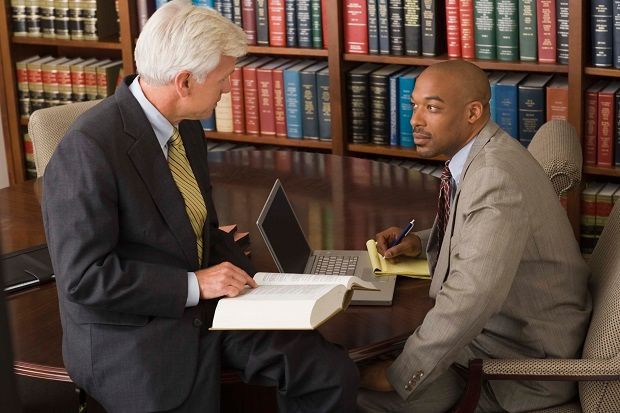 Two people in a library discuss documents at a table with a laptop and books.