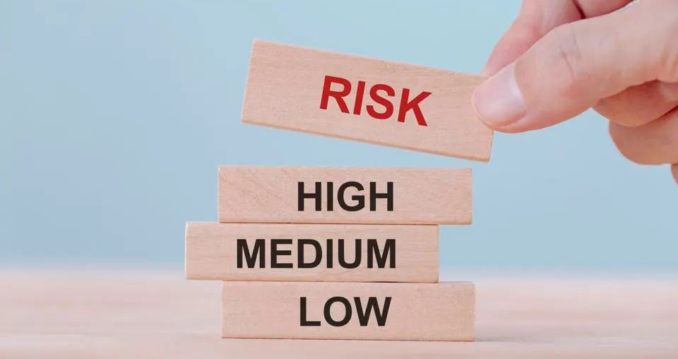 Hand placing a “RISK” block atop a stack labeled low, medium, and high on a blue background