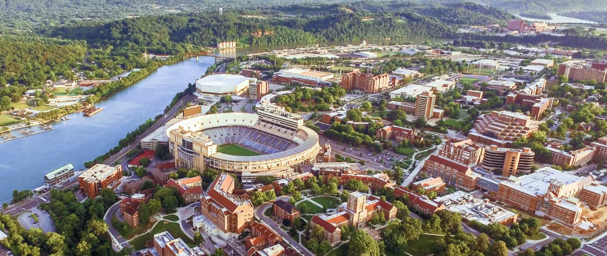 Aerial view of a lush riverside town with a stadium, buildings, and a winding river