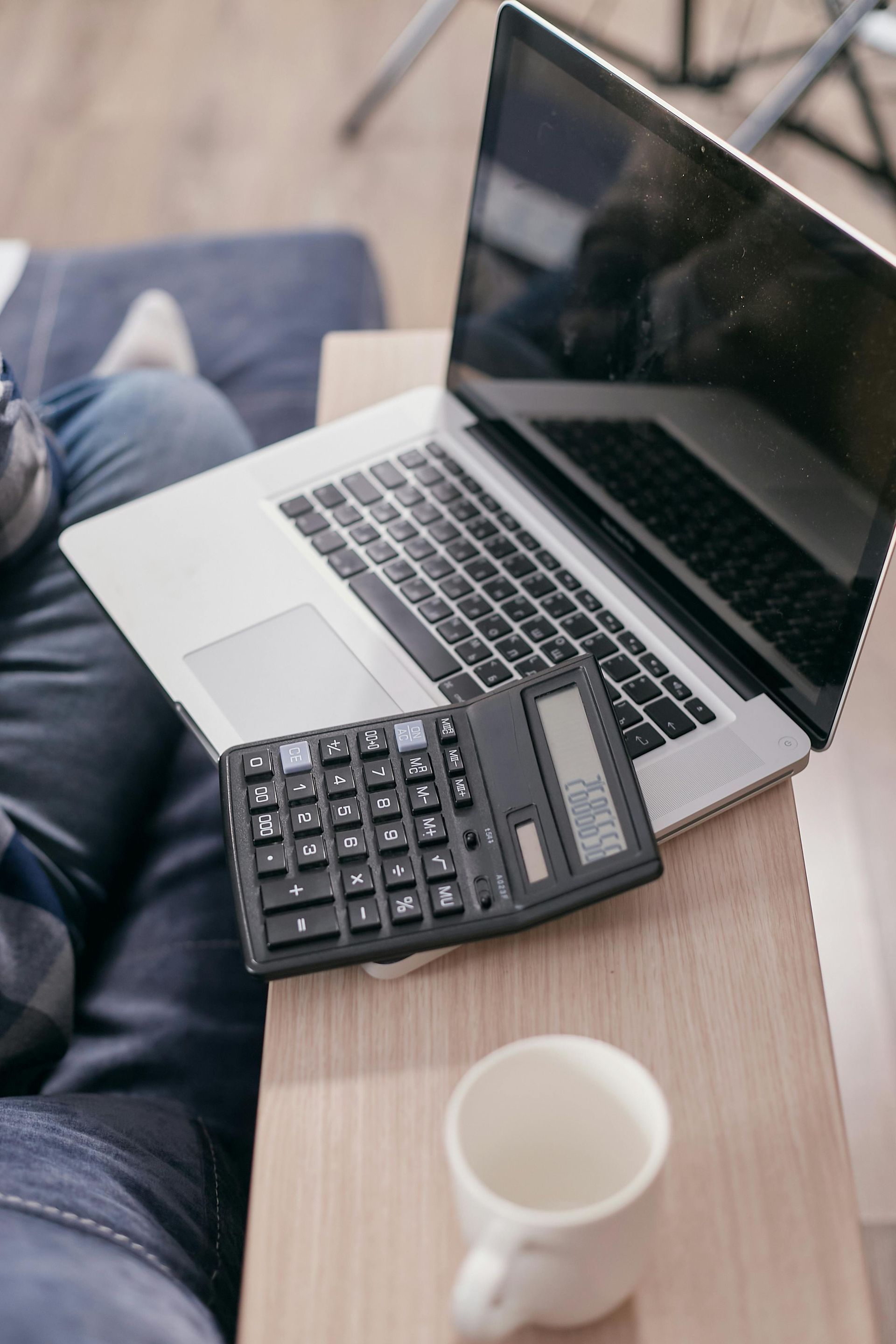 Laptop on a wooden table with a calculator and a small white cup nearby