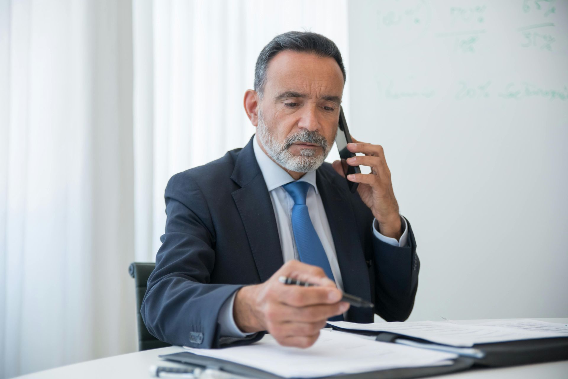 Businessman in a suit talking on a phone while reviewing documents at a desk