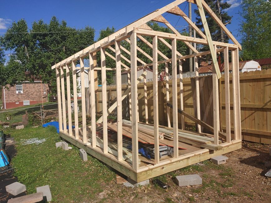 Partially built wooden shed frame in a sunny backyard with a fence and scattered blocks around it